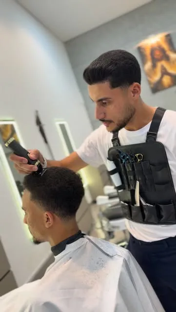 Barbeiro com coldre de ferramentas passando a máquina na lateral de um cliente