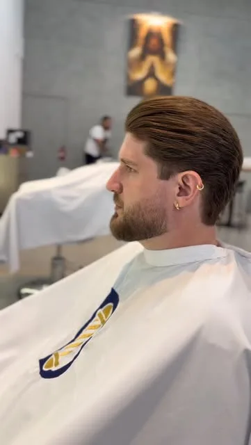 Cliente de perfil com degradê nas laterais e barba alinhada, de capa branca com o logo B